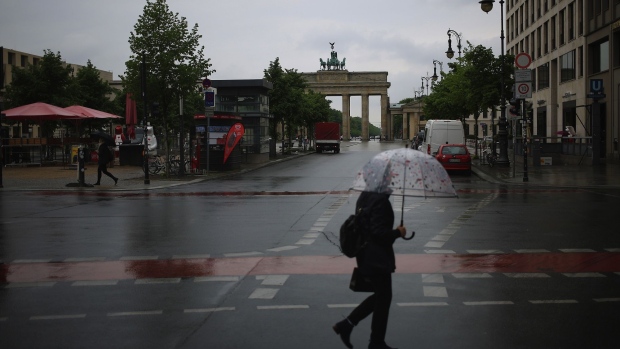A pedestrian shelters under an umbrella while crossing Unter den Linden boulevard near the Brandenburg Gate monument in Berlin, Germany, on Monday, May 4, 2020. Germany reported the lowest number of new coronavirus infections and deaths since at least March 30, as the country continues a gradual easing of curbs on public life and allows the economy to slowly restart. Photographer: Krisztian Bocsi/Bloomberg