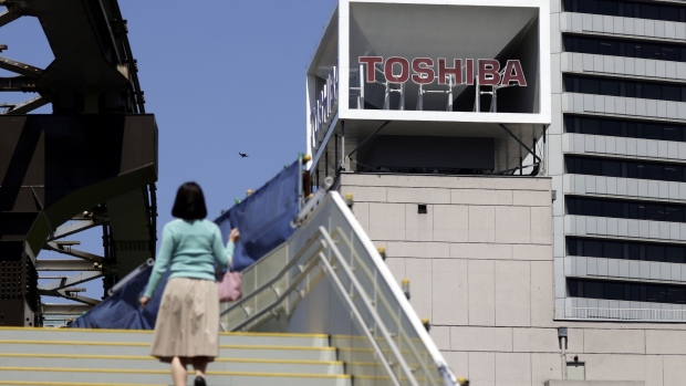 A pedestrian walks up a flight of stairs near signage for Toshiba Corp. displayed at the company's headquarters in Tokyo, Japan, on Wednesday, April 7, 2021. Toshiba surged its daily limit of 18% after confirming it received an initial buyout offer from CVC Capital Partners, setting the stage for potentially the largest private equity-led acquisition in years.