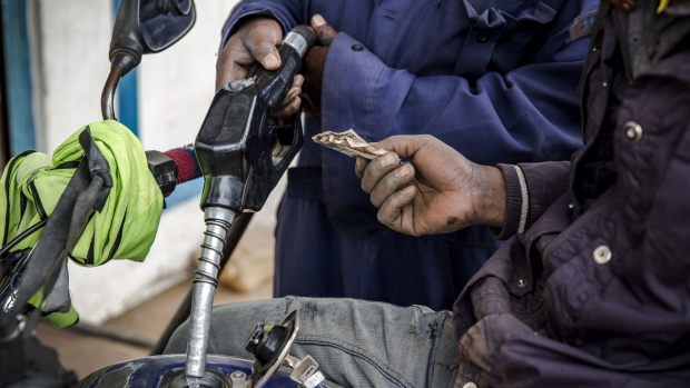 An attendant refuels a motorcycle taxi, known locally as a 'boda boda', as a customer hands Kenyan shilling banknotes over for payment at the Euro Petroleum petrol station in the Baba Dogo suburb of Nairobi, Kenya.