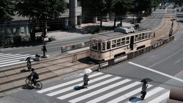 Pedestrians and a cyclist cross a street passing a tram in Kumamoto, Japan, on Wednesday, May 18, 2022. Japan is scheduled to release its consumer price index (CPI) figures for March on May 20.