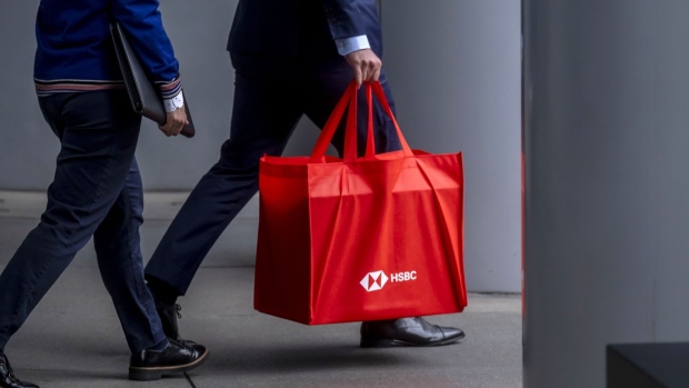 A commuter carrying a bag with the HSBC Holdings Plc logo walks underneath the bank's headquarters building in the Central district of Hong Kong, China, on Monday, June, 7, 2021. Goldman Sachs Group Inc. and HSBC are opening their offices fully in Hong Kong as a fourth wave of infections was contained and the U.S. investment bank said half of its staff in the financial hub are now vaccinated. Photographer: Paul Yeung/Bloomberg