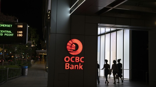 Pedestrians pass in front of Oversea-Chinese Banking Corp. (OCBC) signage illuminated at night in the shopping district of Singapore, on Tuesday, March 24, 2020. Singapore will deliver a supplementary budget and bring forward its monetary policy decision as authorities ramp up support for an economy heading toward recession. Photographer: Wei Leng Tay/Bloomberg
