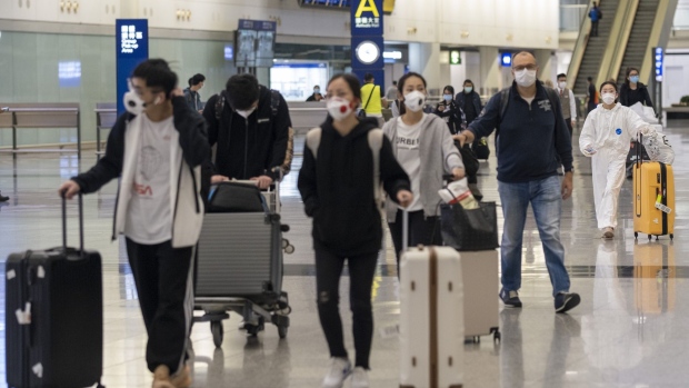 Travelers wearing protective masks walk with luggage through the arrivals hall of Hong Kong International Airport (HKG) in Hong Kong, China, on Wednesday, March 18, 2020. Hong Kong found 14 new confirmed coronavirus cases, according to the Department of Health. This is the biggest daily jump on record, according to data compiled by Bloomberg, and brings the total confirmed cases to 181. Photographer: Justin Chin/Bloomberg