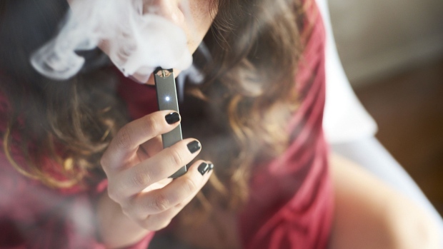 A person smokes a Juul Labs Inc. e-cigarette in this arranged photograph taken in the Brooklyn Borough of New York, U.S., on Sunday July 8, 2018. Juul Labs, the maker of the popular e-cigarette brand that has recently come under fire from health officials over its popularity with young adults, plans to introduce a line of lower-nicotine pods. The company will begin to sell pods with a 3-percent nicotine concentration in its mint and Virginia tobacco flavors later this year, according to a statement Thursday.