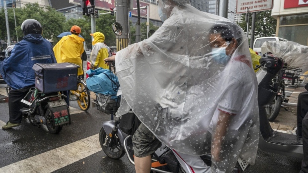 BEIJING, CHINA -JUNE 27: A student is covered in his parent's raincoat as they drive in the rain on a scooter to school as many schools reopened on June 27, 2022 in Beijing, China. China's capital had closed its schools in late April as part of the government's efforts to control recent outbreaks of COVID-19 and maintain its zero COVID policy. (Photo by Kevin Frayer/Getty Images)