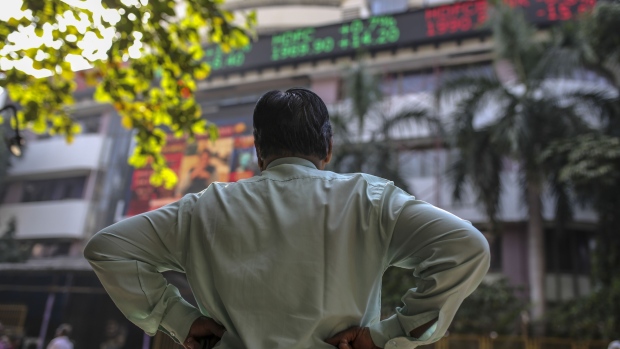 A man stands in front of an electronic ticker board showing stock information figures outside the Bombay Stock Exchange (BSE) in Mumbai. Photographer: Dhiraj Singh/Bloomberg