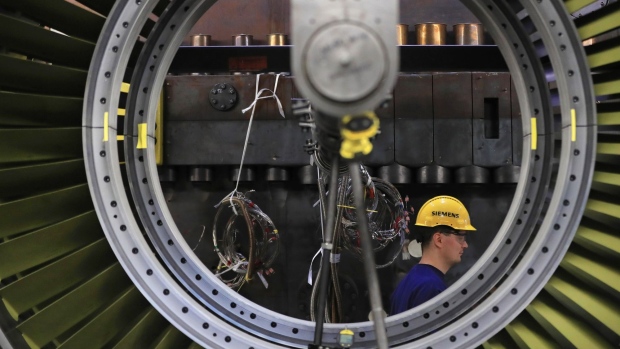 A worker wearing a branded yellow hard hat walks by a SGT5-4000F gas turbine inside a Siemens AG gas turbine factory in Berlin, Germany, on Wednesday, Dec. 4, 2019. Siemens AG aims to shed about 75% of its struggling power and gas unit in one of the most radical moves to date by Chief Executive Officer Joe Kaeser to untangle the sprawling conglomerate and try to boost its valuation. Photographer: Krisztian Bocsi/Bloomberg