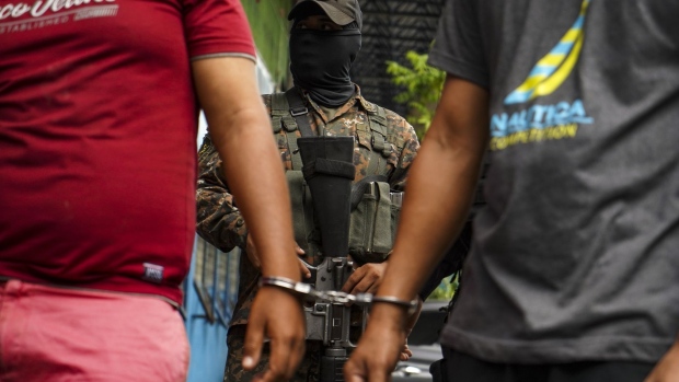 A member of the military stands guard behind two alleged gang members who have been handcuffed in San Salvador, El Salvador, on Monday, April 25, 2022. El Salvadoran lawmakers granted President Nayib Bukele another 30 days of emergency powers Sunday, after a crackdown that he says has enabled the arrest of 16,000 alleged gang members.
