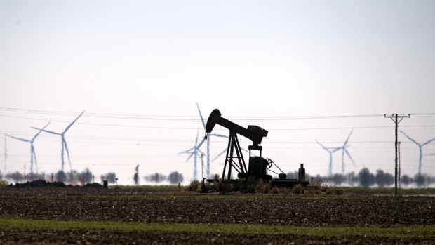 A pump jack stands next to wind turbines near Guymon, Oklahoma, U.S., on Friday, Sept. 25, 2020. After all the trauma the U.S. oil industry has been through this year -- from production cuts to mass layoffs and a string of bankruptcies -- many producers say they’re still prioritizing output over reducing debt.
