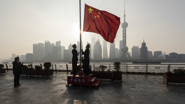 China Customs officers raise a Chinese flag during a rehearsal for a flag-raising ceremony along the Bund in front of buildings in the Lujiazui Financial District at sunrise in Shanghai, China, on Tuesday, Jan. 4, 2022. A wall of maturing debt and a surge in seasonal demand for cash will test China’s financial markets this month, putting pressure on the central bank to ensure sufficient liquidity. Photographer: Qilai Shen/Bloomberg