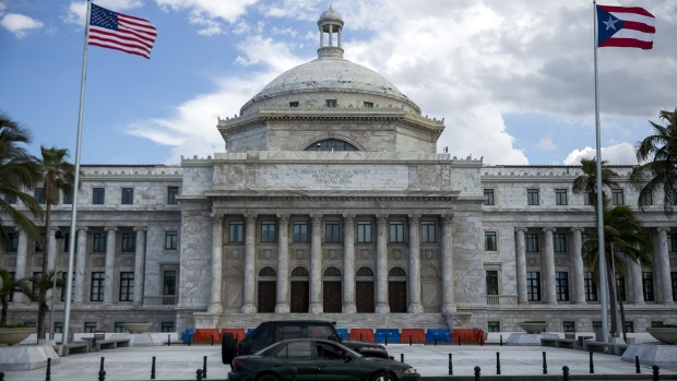 American and Puerto Rican flags fly outside the Capitol of Puerto Rico building in San Juan, Puerto Rico, on Saturday, May 13, 2017. With Wall Street's help, the U.S. commonwealth borrowed tens of billions in the bond markets, only to squander much of it on grand projects, government bureaucracy, everyday expenses and worse. Debts were piled on debts, even as the economy gave way.