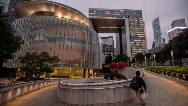 A pedestrian walks past the Legislative Council building, left, and the Central Government Offices, center, at dusk in Hong Kong, China, on Tuesday, Nov. 23, 2021. Hong Kong's border with mainland China won't fully reopen before next month's vote on the local legislature, the city's leader said, as officials from both sides work to restore economically crucial ties. Photographer: Paul Yeung/Bloomberg