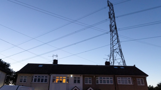 An electricity transmission tower near residential houses with lights on in Upminster, UK, on Monday, July 4, 2022. The UK is set to water down one of its key climate change policies as it battles soaring energy prices that have contributed to a cost-of-living crisis for millions of consumers. Photographer: Chris Ratcliffe/Bloomberg