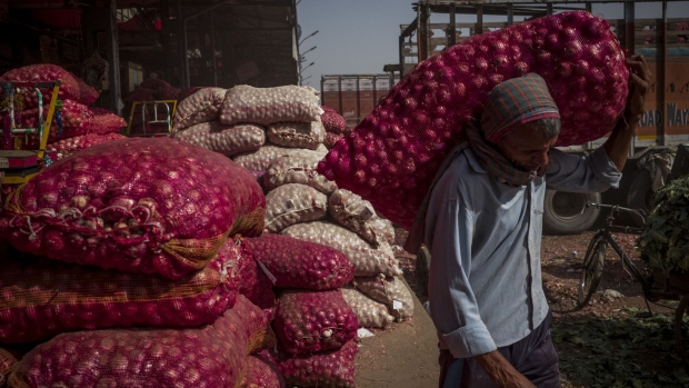 A worker carries a sack of onions from a stack of onions and potatoes at the Azadpur wholesale market in New Delhi, India, on Sunday, June 5, 2022. India's Ministry of Agriculture data show tomato price inflation surged to 61% month on month in May. Even so, other vegetable prices have come down sharply from elevated levels in April. Photographer: Anindito Mukherjee/Bloomberg