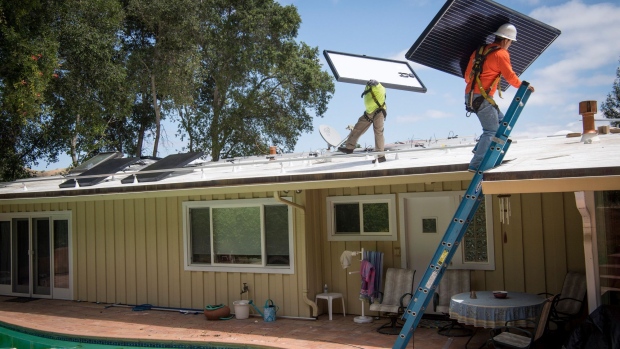 PetersenDean Inc. employees carry solar panels onto the roof of a home in Lafayette, California, U.S., on Tuesday, May 15, 2018. California became the first in the U.S. to require solar panels on almost all new homes. Most new units built after Jan. 1, 2020, will be required to include solar systems as part of the standards adopted by the California Energy Commission.
