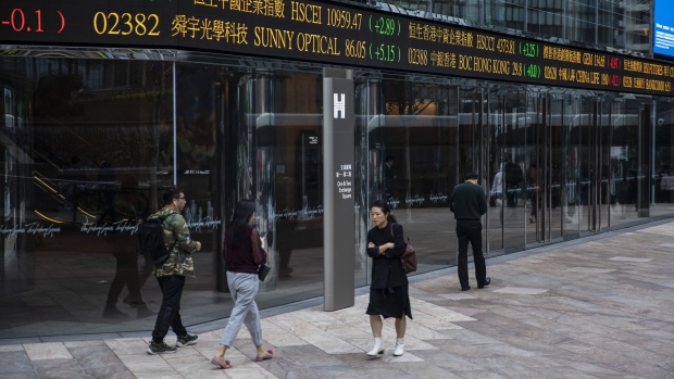 Pedestrians walk past an electronic ticker board displaying stock figures outside the Exchange Square complex, which houses the Hong Kong Stock Exchange, in Hong Kong, China, on Monday, Feb. 11, 2019. The bullish mood building in China’s equity market is entering a new phase, with investors flocking to riskier stocks as trading reopened Monday.