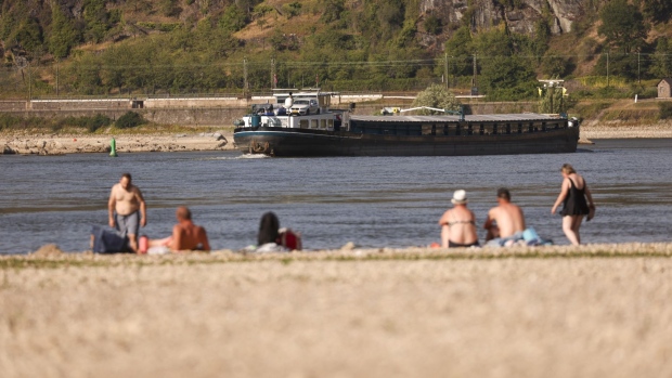 A barge passes residents on an exposed riverbed on the River Rhine near Loreley, Germany, on Friday, Aug. 12, 2022. The Rhine River fell to a new low on Friday, further restricting the supply of vital commodities to parts of inland Europe as the continent battles with its worst energy crisis in decades.