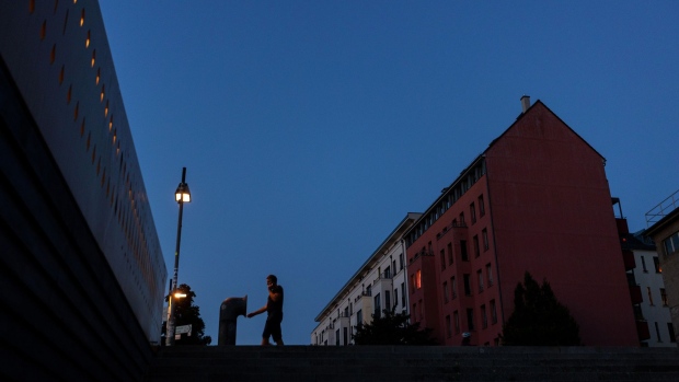 A street lamp lights a resident outside partially lit blocks of apartments at dusk in Berlin, Germany, on Tuesday, Aug. 16, 2022. Germany's government has asked citizens, municipalities and industrial consumers to save energy, and efforts can be seen across the country.
