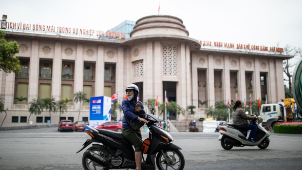 A woman looks back while sitting on a motorcycle in front of the State Bank of Vietnam in Hanoi, Vietnam, on Monday, Feb. 25, 2019. U.S. President Donald Trump and North Korean leader Kim Jong Un are scheduled to meet between Wednesday and Thursday in Hanoi for their second summit. Photographer: SeongJoon Cho/Bloomberg