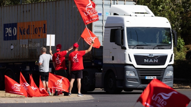 Striking Unite union members and dockworkers wave placards as trucks leave the Port of Felixstowe in Felixstowe, UK, on Wednesday, Aug. 24, 2022. The Felixstowe strike -- one of many that have broken out across the UK -- is upending supply chains in the country as goods are left unprocessed and undelivered.
