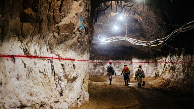Miners walk through an underground tunnel illuminated with lights at the South Deep gold mine, operated by Gold Fields Ltd., in Westonaria, South Africa, on Thursday, March 9, 2017. South Deep is the world's largest gold deposit after Grasberg in Indonesia, makes up 60 percent of the company's reserves and the miner says it's capable of producing for 70 years.