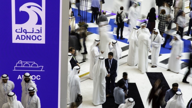 Delegates pass the Abu Dhabi National Oil Co. (ADNOC) display during the Abu Dhabi International Petroleum Exhibition & Conference (ADIPEC) in Abu Dhabi, United Arab Emirates, on Tuesday, Nov. 13, 2018. OPEC’s secretary-general, energy ministers from Saudi Arabia to Russia, CEOs at oil majors from Total SA, BP Plc and Eni SpA, and officials from Middle Eastern energy giants such as Abu Dhabi’s Adnoc have gathered to sign deals and discuss oil, gas, refining and petrochemical issues. Photographer: Christopher Pike/Bloomberg