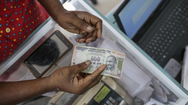 A customer holds Indian one hundred rupee banknote at the Mayuresh Watches and Traders watch and mobile phone store in the Byculla area of Mumbai, India, on Monday, Jan. 29, 2018. Hundreds of thousands of Indian shopkeepers are making money transfers, deposits, and withdrawals on behalf of customers at all hours of the day and even late into the night. Corner shops, tailors, pharmacies, and even doctors' offices are adding these simple financial services as a lucrative new sideline.
