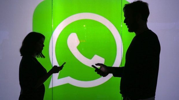 People are seen as silhouettes as they check mobile devices whilst standing against an illuminated wall bearing WhatsApp Inc's logo in this arranged photograph in London, U.K., on Tuesday, Jan. 5, 2016. WhatsApp Inc. offers a cross-platform mobile messaging application that allows users to exchange messages. Photographer: Bloomberg/Bloomberg