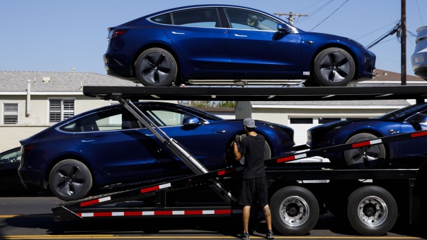 Workers unload Tesla Model 3 electric vehicles from a car carrier outside the company's delivery center in Marina Del Rey, California.