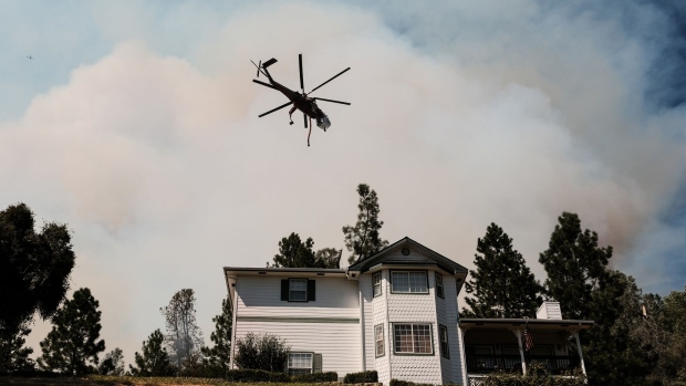 A helicopter flies over a fire near a home situated on Pinecrest drive during the Oak Fire in Mariposa County, California, US, on Saturday, July 23, 2022. A fast-moving wildfire near Yosemite National Park exploded in size Saturday into one of California's largest wildfires of the year, prompting evacuation orders for thousands of people and shutting off power to more than 2,000 homes and businesses.