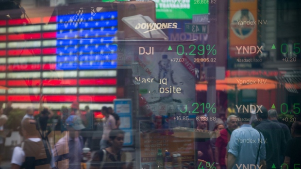 Monitors display stock market information as pedestrians are reflected in a window at the Nasdaq MarketSite in the Times Square area of New York.