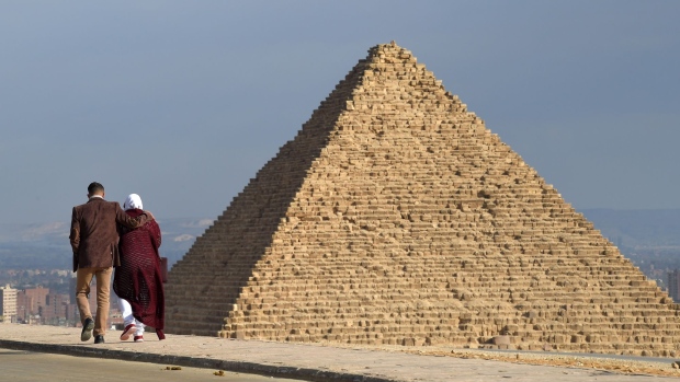 A couple walk along a road at the Giza pyramids necropolis on the southwestern outskirts of the Egyptian capital Cairo. Photographer: Mohamed El-Shahed/AFP/Getty Images
