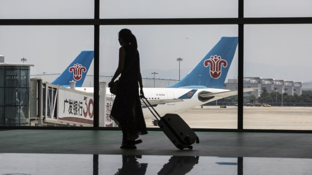 A woman carrying luggage is silhouetted as she walks past aircraft operated by China Southern Airlines Co. sitting on the tarmac at Terminal 2 of the Guangzhou Baiyun International Airport in Guangzhou, China, on Saturday, May 19, 2018. China Southern will ramp up flights to Europe and North America from the country's top-tier cities to challenge the dominance of rival Air China Ltd. Photographer: Qilai Shen/Bloomberg
