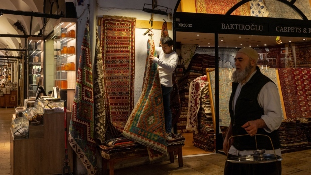 A shopkeeper hangs carpets outside his store at the Grand Bazaar in Istanbul. Photographer: Nicole Tung/Bloomberg