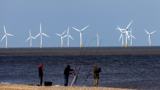 Offshore wind turbines beyond fishermen on the beach at the Scroby Sands Wind Farm, operated by E.ON SE, near Great Yarmouth, UK, on Friday, May 13, 2022. The U.K. will introduce new laws for energy to enable a fast build out of renewables and nuclear power stations as set out in the government’s energy security strategy last month. Photographer: Chris Ratcliffe/Bloomberg