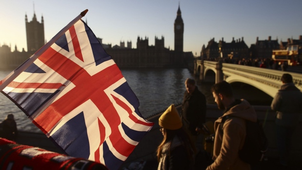 Tourists walk past a souvenir stall selling British Union flags beside Westminster Bridge on the River Thames in view of the Houses of Parliament in London, U.K., on Thursday, Dec. 29, 2016. Demand for luxury brands in the U.K. is flourishing, boosted by increased tourism and spending linked to the weaker pound.