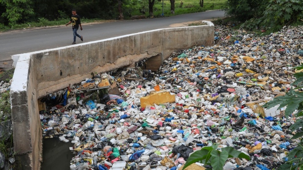 A pedestrian walks along a bridge over a gutter, blocked by plastic waste and garbage, in Accra, Ghana, on Monday, July 4, 2022. Love it or hate it, plastic is a matter of life and death in Ghana, a nation of 32 million where a quarter of the population lives in poverty and many citizens can’t cook with what comes from their taps without risking sickness.