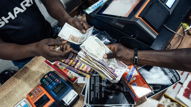 A customer hands over Nigerian naira banknotes in a store in Abuja, Nigeria, on Friday, Jan. 10, 2020. Revenue in Nigeria has fallen short of the government target by at least 45% every year since 2015, and shortfalls have been funded through increased borrowing. Photographer: KC Nwakalor/Bloomberg