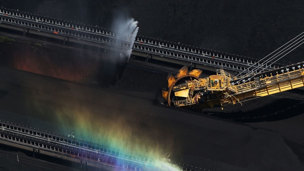 A stacker-reclaimer operates next to stockpiles of coal as a rainbow forms in a spraying jet of water at the Newcastle Coal Terminal in this aerial photograph taken in Newcastle, Australia. Photographer: Brendon Thorne/Bloomberg