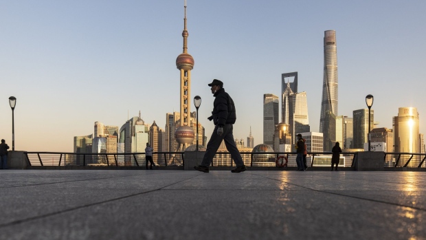A pedestrian walks along the Bund past buildings in the Lujiazui Financial District in Shanghai, China, on Tuesday, Dec. 28, 2021. China’s economy expanded at a moderate pace in the final month of the year, supported by better business sentiment, easing factory inflation pressures and faster car sales. However the slumping property sector and slowing external demand are clouding the outlook for the world’s second-largest economy. Photographer: Qilai Shen/Bloomberg
