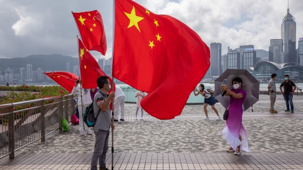 A man poses for a photograph with a flag of China while celebrating Chinese National Day at Tsim She Tsui in Hong Kong, China, on Saturday, Oct. 1, 2022. Hong Kong is slowly unwinding some of its toughest pandemic rules, which had kept it in line with mainland China’s Covid Zero policies but devastated the city’s economy and sparked an exodus of residents. Photographer: Paul Yeung/Bloomberg