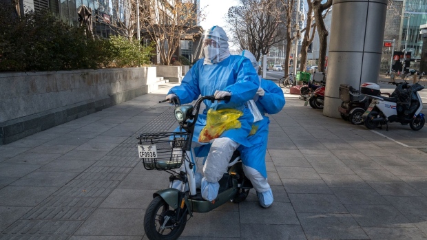 Medical workers in protective gear ride an e-bike in Beijing, China, on Tuesday, Dec. 13. 2022. China's abrupt ending of its Covid Zero policy injects more uncertainty into an already fragile economy, raising the prospect of looser fiscal and monetary policy and more easing in the property market to bolster growth.