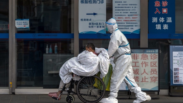 A health worker in protective gear pushes a patient on a wheelchair at a hospital in Beijing, China, on Wednesday, Dec. 14, 2022. Covid infections are surging in Beijing, disrupting official government work and keeping people at home after authorities made an about-turn in their policy of keeping virus cases under control.