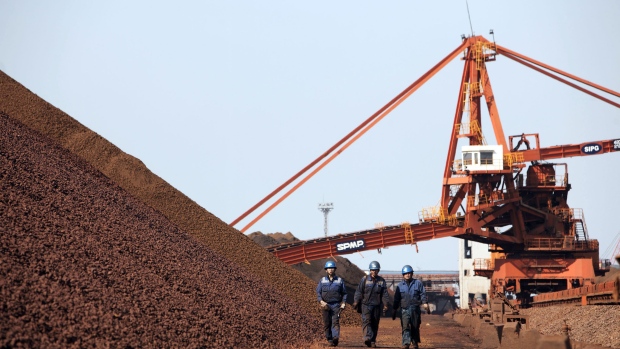 Workers walk past piles of iron ore in Shanghai, China. Photographer: Qilai Shen/Bloomberg