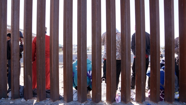 Migrants wait at the US and Mexico border wall in El Paso, Texas, on Dec. 22, 2022. Photographer: Eric Thayer/Bloomberg