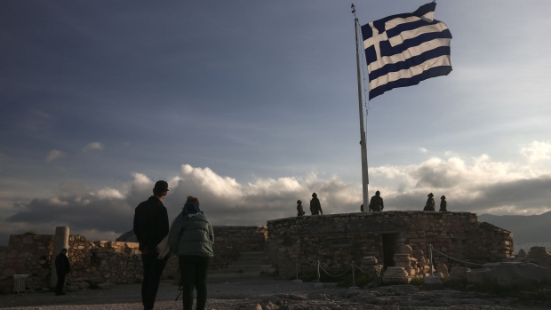 Tourists watch Greek army soldiers raise the national flag on Acropolis Hill in Athens, Greece, on Thursday, Feb. 9, 2017. Greece is back in the headlines as it struggles to free itself from a disagreement between the International Monetary Fund and Europe. Photographer: Yorgos Karahalis/Bloomberg