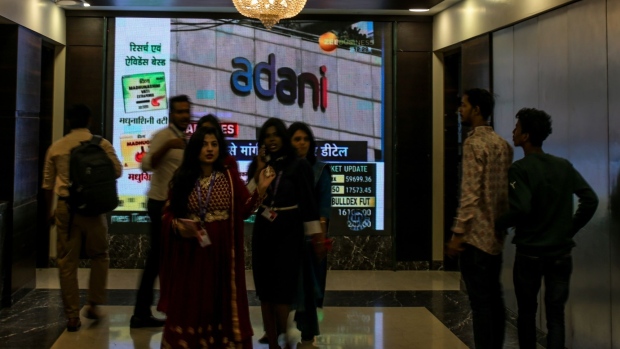 People walk past a screen displaying news featuring on Adani Group inside the BSE building in Mumbai, India, on Thursday, Feb. 2, 2023. Adani’s businesses have lost $107 billion in a week, one of the biggest wipeouts in India’s history, after an explosive report by short-seller Hindenburg Research forced him to pull a stock sale at the 11th hour and led some lenders to reject his securities as collateral for client trades.