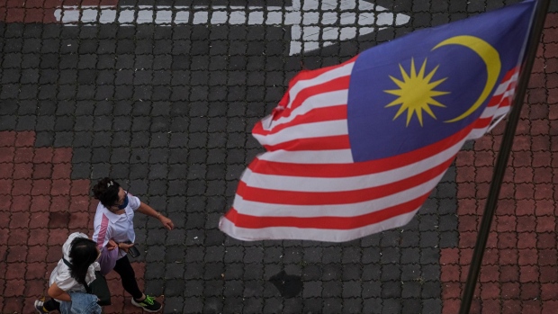 Pedestrians walk past a Malaysian flag outside the Ipoh International Convention Centre in Ipoh, Perak, Malaysia, on Thursday, Oct. 20, 2022. Malaysia will hold elections on Nov. 19 with Prime Minister Ismail Sabri Yaakob's party looking to capitalize on a string of victories from local polls and consolidate power in the Southeast Asian country. Photographer: Samsul Said/Bloomberg