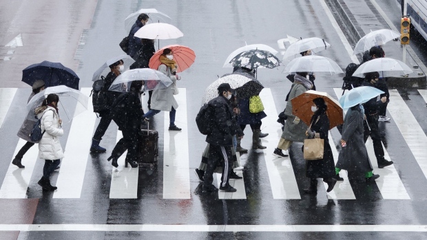Morning commuters holding umbrellas cross a road in the Shinjuku district of Tokyo, Japan, on Thursday, Feb. 10, 2022. Japan’s wholesale power rate spiked as a forecast for potentially heavy snow in the nation’s capital this week may boost heating demand. Photographer: Kiyoshi Ota/Bloomberg
