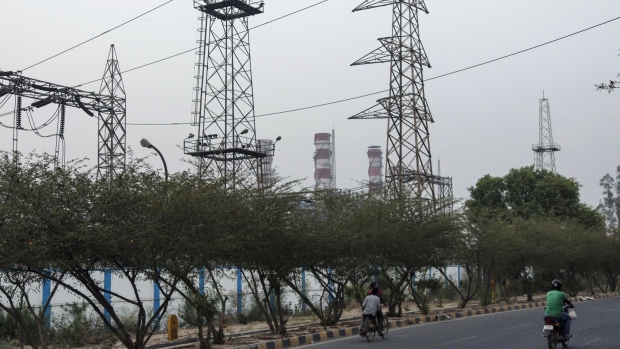 A motorcycist and cyclist ride along a highway under power lines hanging from transmission towers at the 1500 Megawatt Combined Cycle Power Station Bawana operated by Pragati Power Corp. (PPCL) in Bawana, Delhi, India on Tuesday, May 3, 2016. About 25 kilometers (16 miles) northwest of Prime Minister Narendra Modi's office in New Delhi, a $780 million gas-fired electricity plant that could reduce the choking pollution in India's capital is operating at a fraction of its potential. The facility ran at about a sixth of capacity on Monday, while a much older, belching coal plant some 15 kilometers southeast of central New Delhi provided the biggest share of the city's power generation. Photographer: Bloomberg/Bloomberg